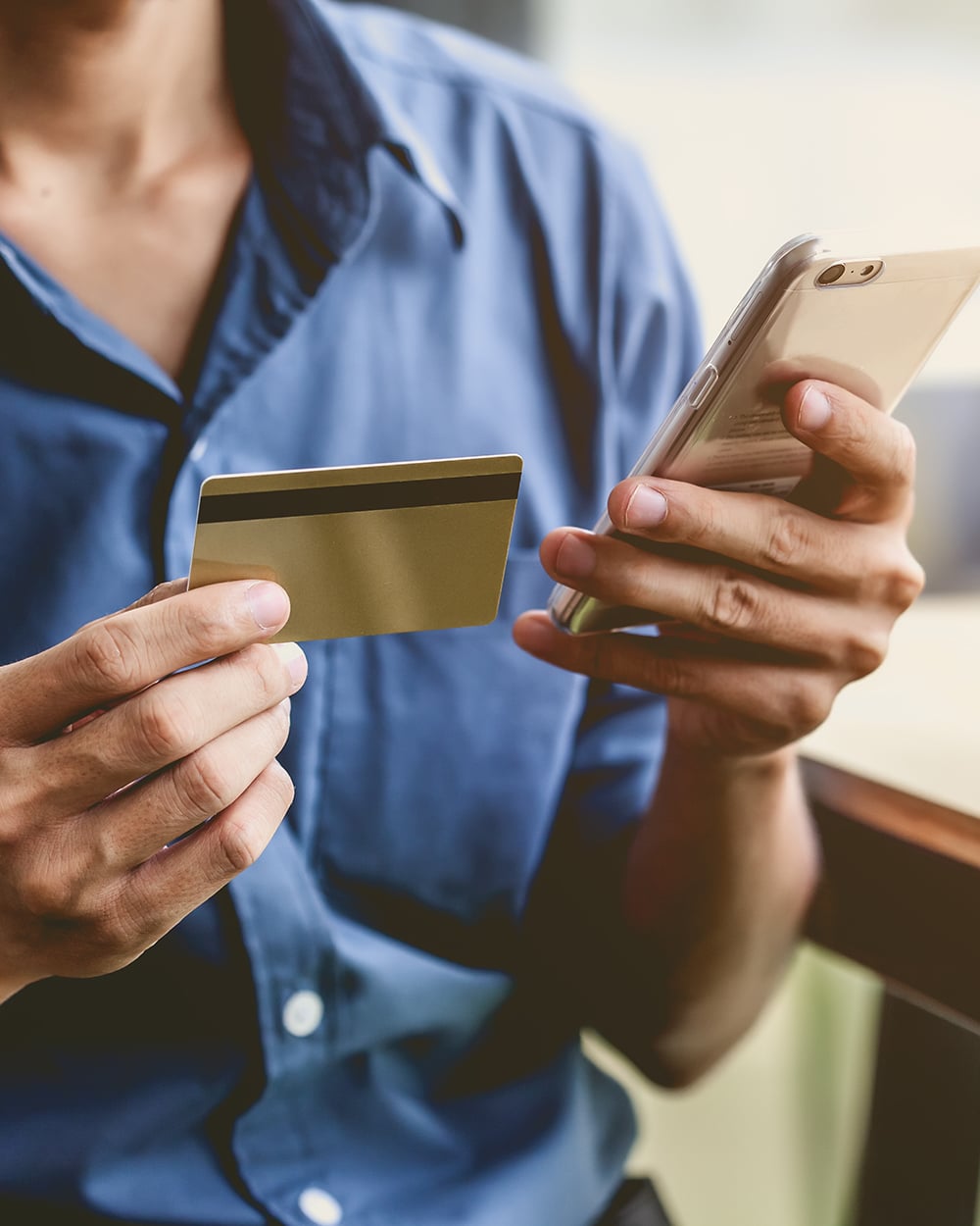 Man wearing a blue shirt uses his credit card to make a payment on his mobile phone